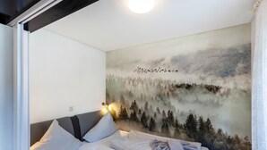 Et soveværelse med seng, puder, sengegavl og et tapet med et skovmotiv.