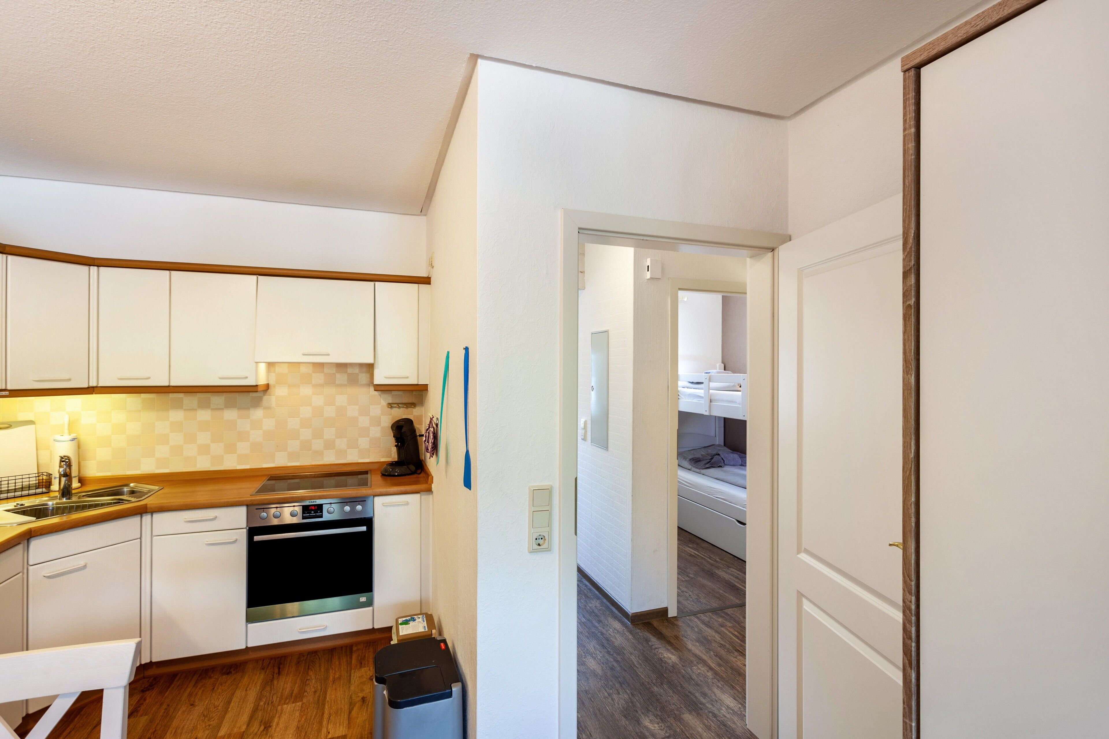 A compact kitchen with white cabinets, a stove, and a trash bin.