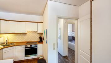 A compact kitchen with white cabinets, a stove, and a trash bin.