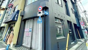 Un bâtiment moderne avec une entrée située à l’angle, un panneau indiquant un passage piéton et un panneau interdisant le stationnement.