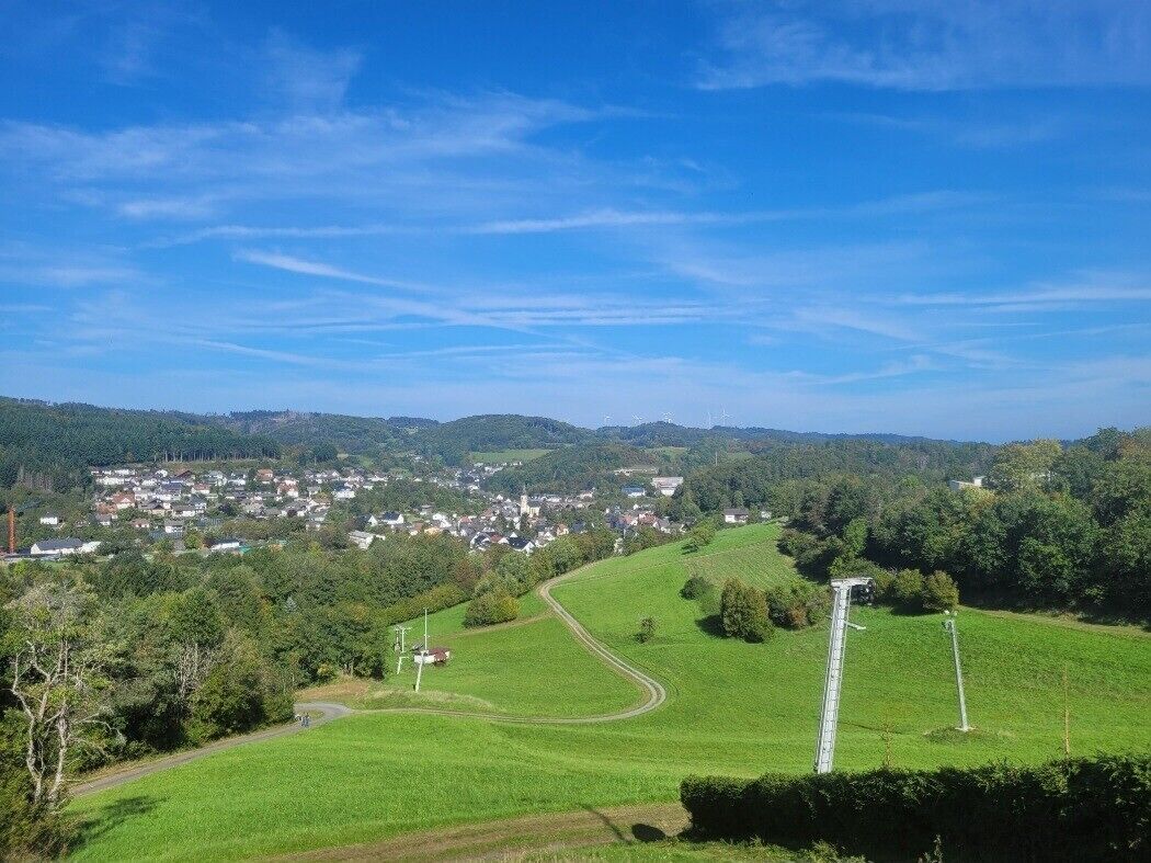 A rural landscape with a winding road, a small village, and a large white structure in the distance.