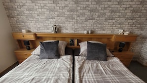 A double bed with a wooden headboard, two bedside tables with lamps, and a brick-patterned wall. - Holiday Apartment "Am Strohberg" with Balcony and Wi-Fi (Gladenbach/ Weidenhausen)
