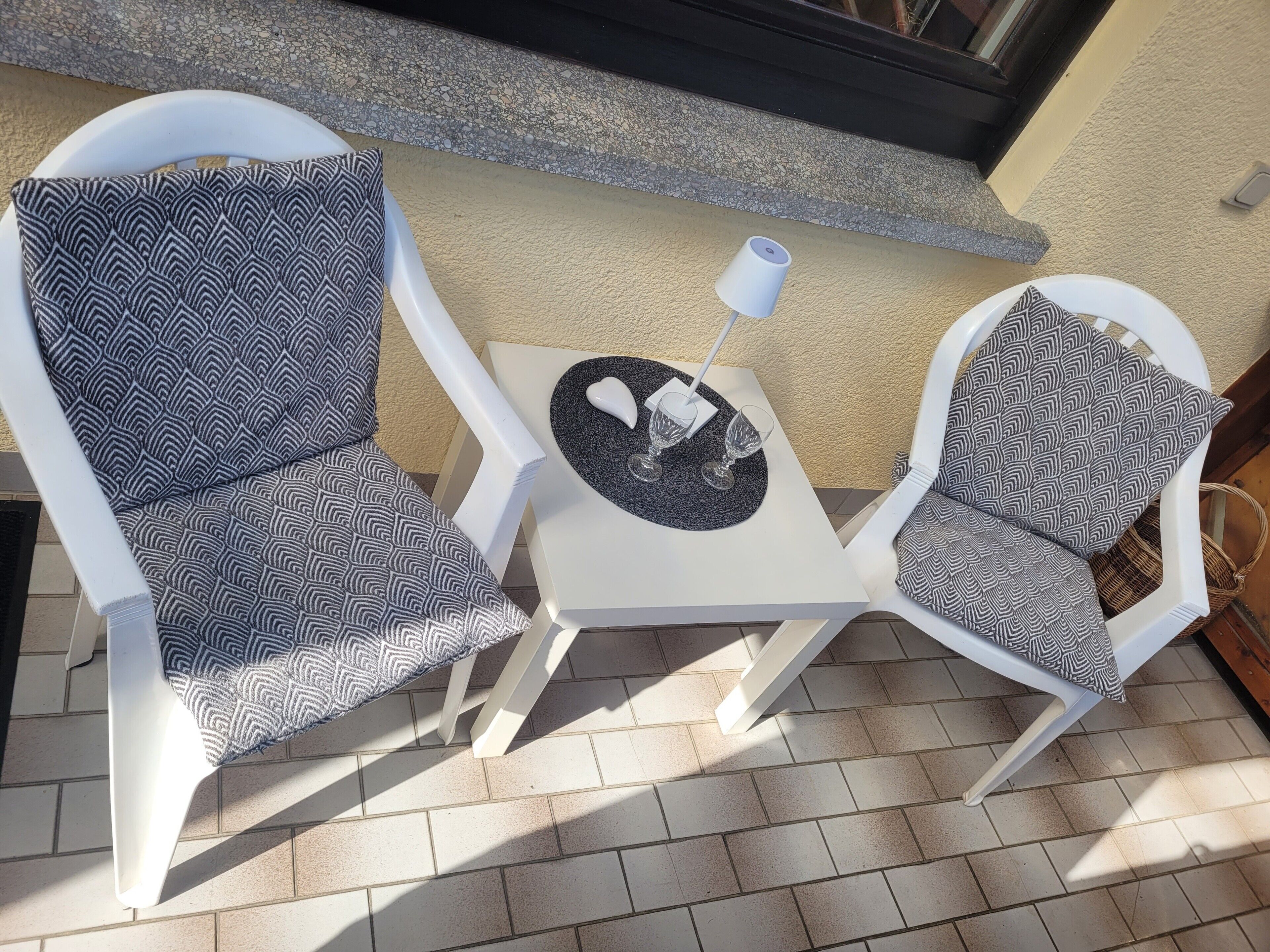 A patio with two white chairs, a small table, and a lamp.