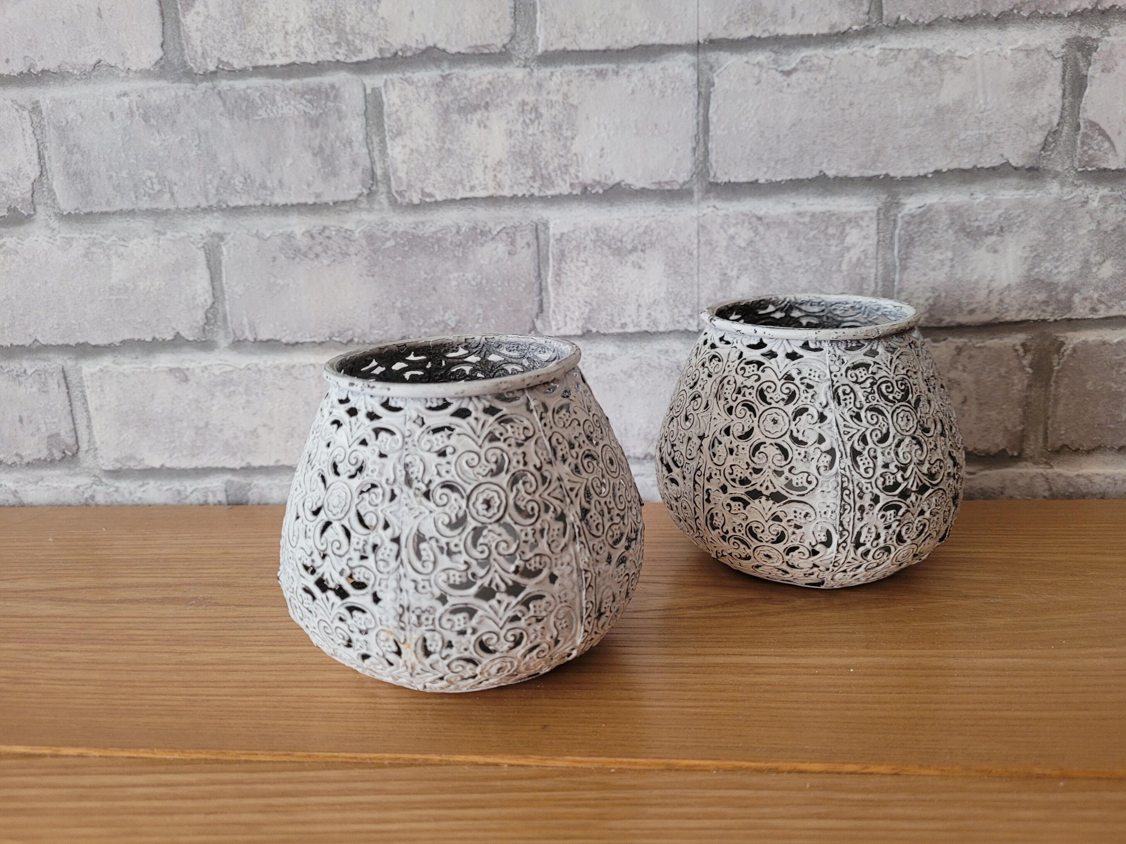 Two intricately patterned ceramic planters on a wooden surface against a brick wall.