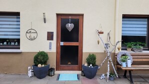 A building entrance with a wooden door, a welcome sign, potted plants, and a bench. - Holiday Apartment "Am Strohberg" with Balcony and Wi-Fi (Gladenbach/ Weidenhausen)