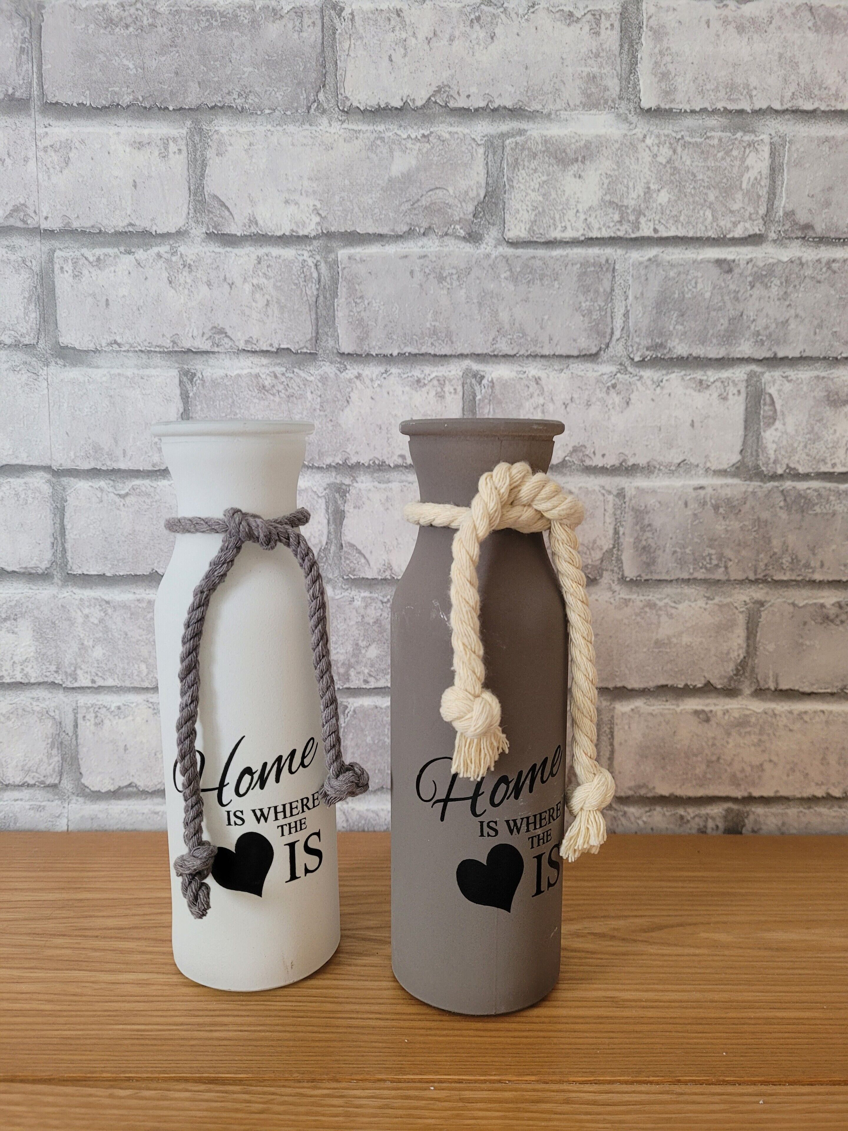Two vases with rope handles and text, placed on a wooden surface against a brick wall.