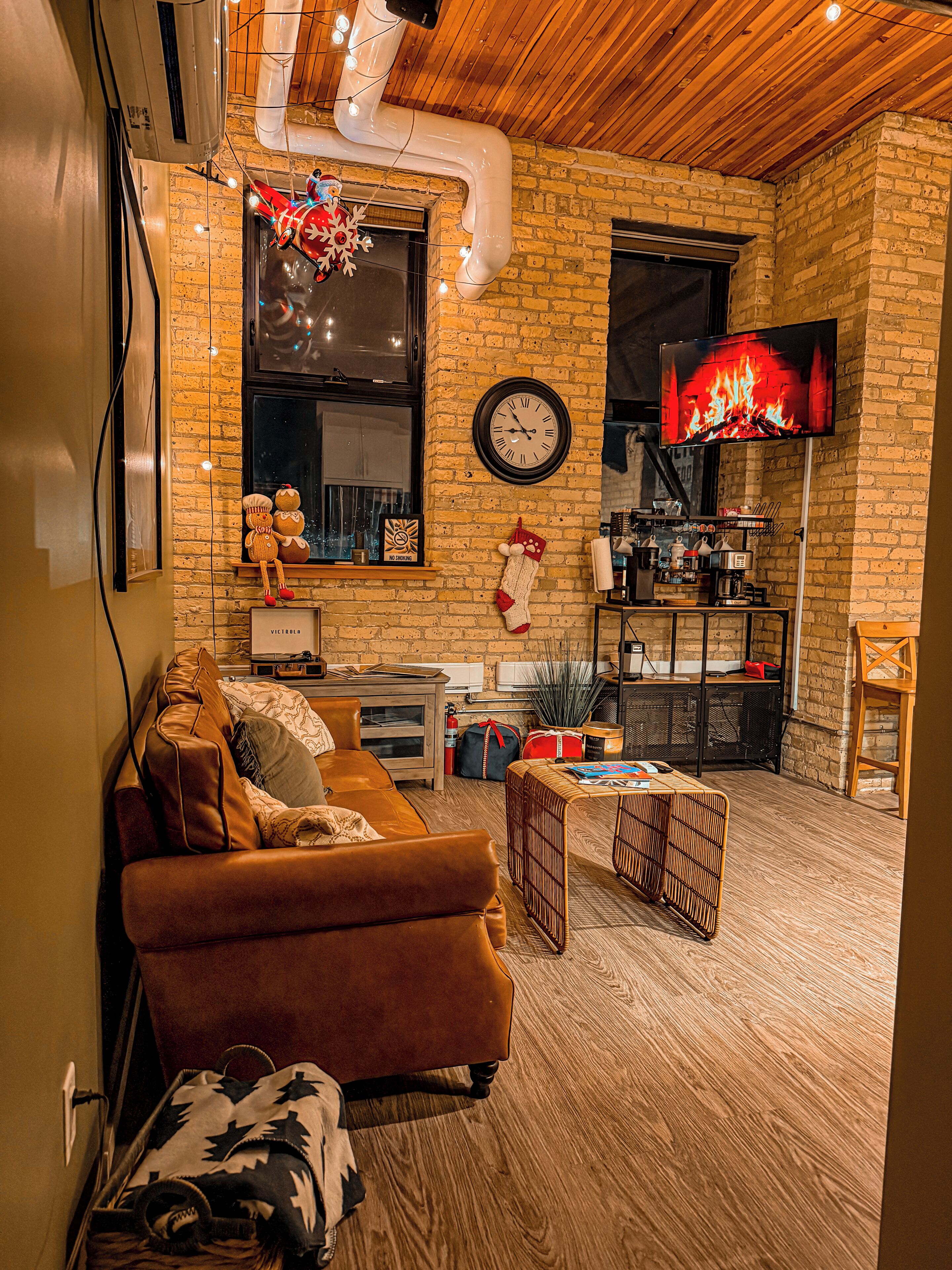 A cozy living room with a brown sofa, a wooden coffee table, and a brick wall.