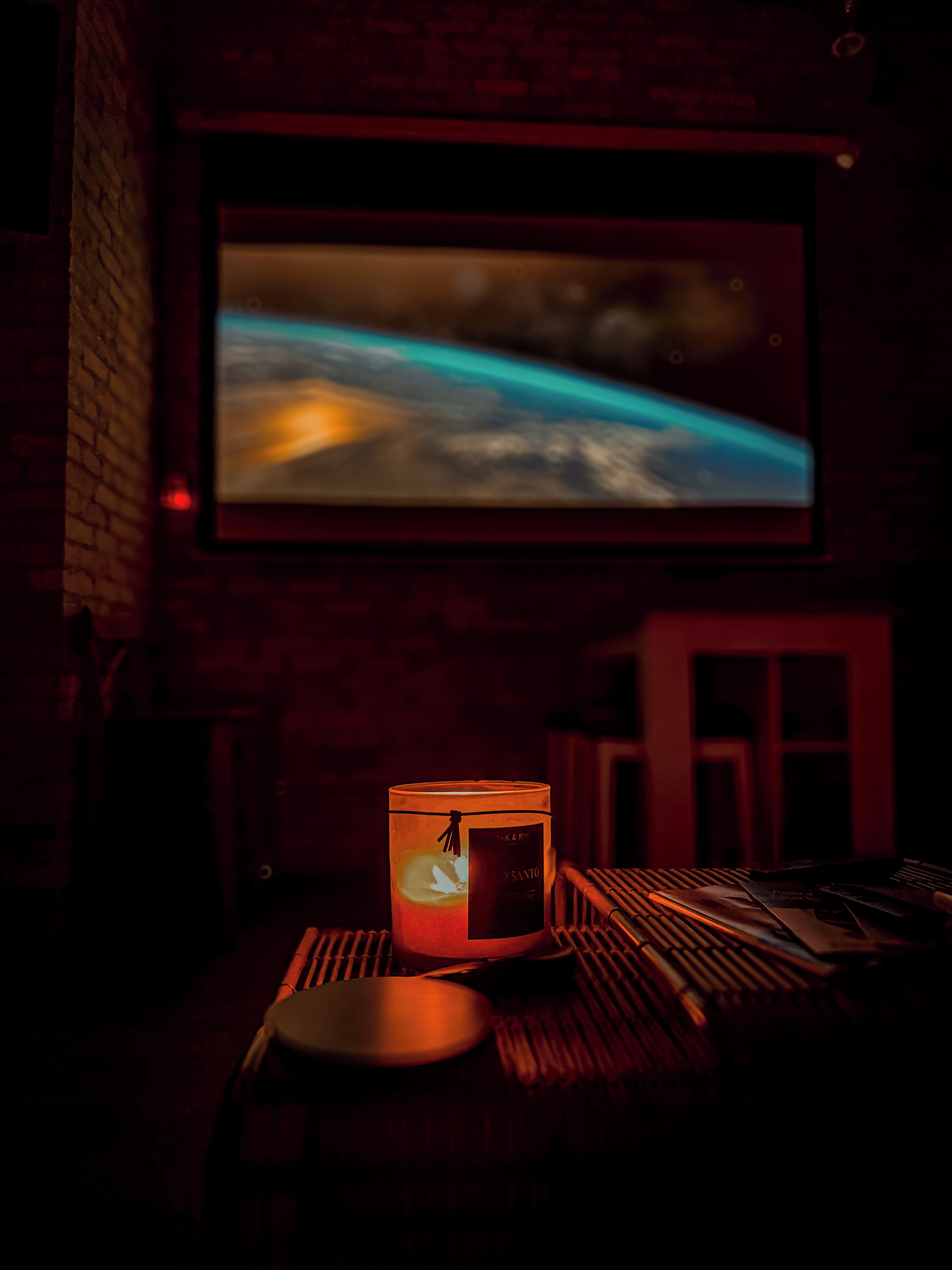 A dimly lit room with a candle on a table, a laptop, and a television displaying a landscape.
