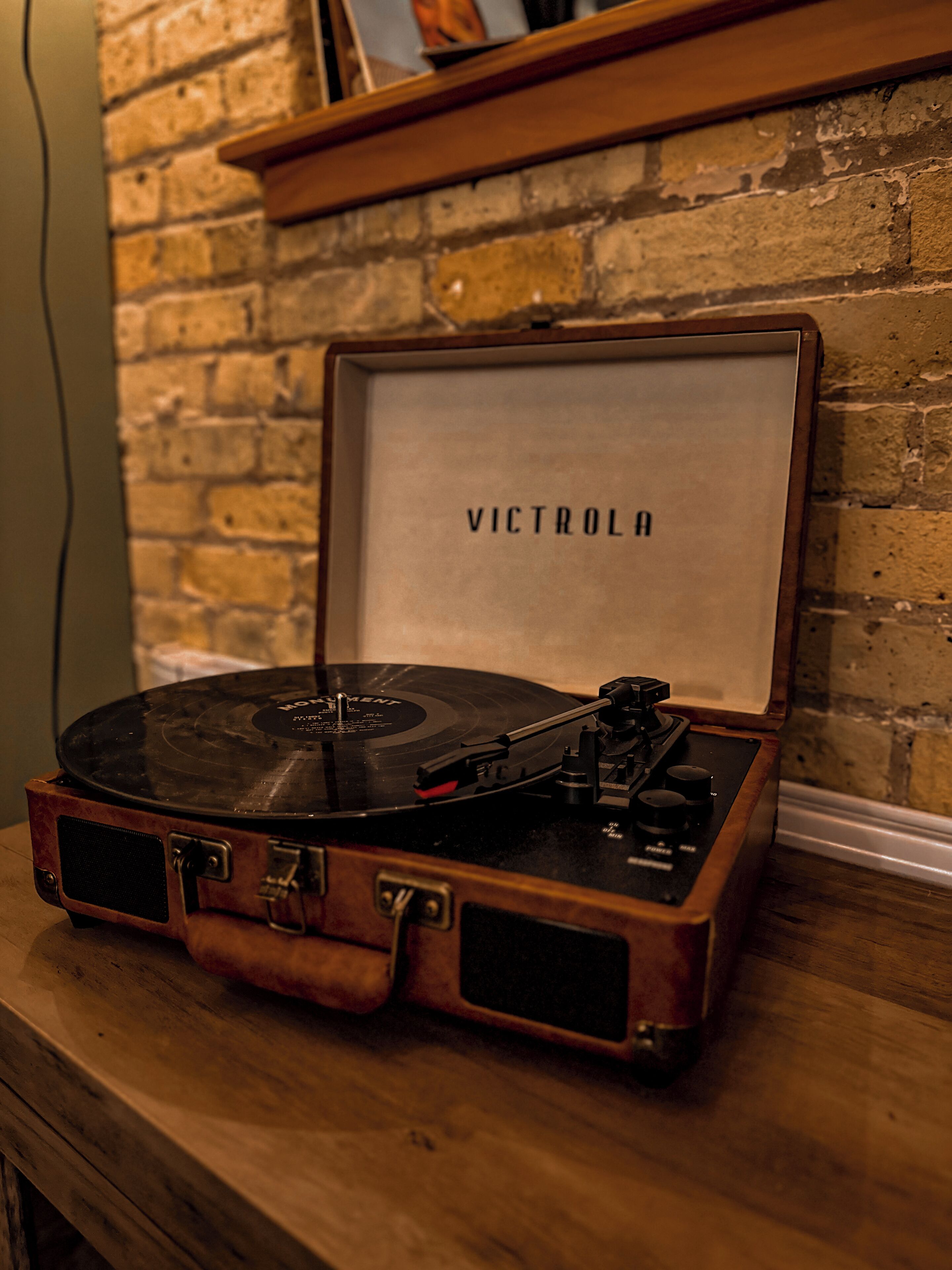 A vintage Victrola record player on a wooden table against a brick wall.