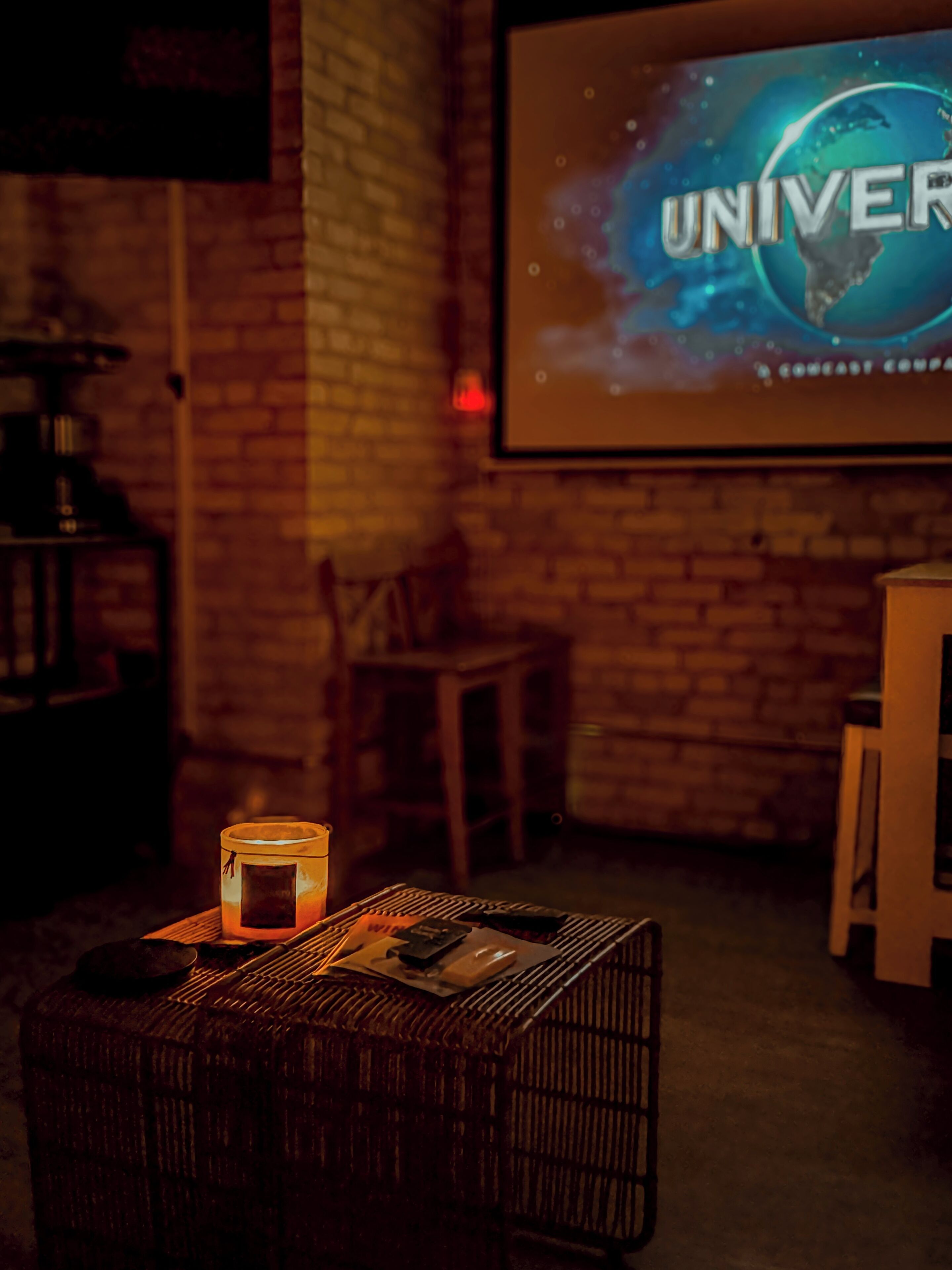 A cozy room with a brick wall, a projector screen displaying the word "UNIVER," a small table with a candle, and a chair.