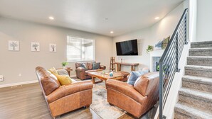A spacious living room with leather sofas, a coffee table, and a TV mounted on the wall. - Berthoud Home w/ Fire Pit, Close to Lake Loveland! (Berthoud)
