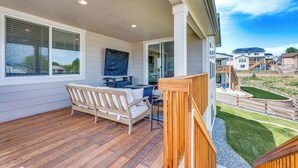 A covered porch with a wooden deck, a white outdoor sofa, and a dining table with chairs. - Berthoud Home w/ Fire Pit, Close to Lake Loveland! (Berthoud)