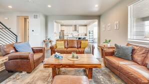 A spacious living room with leather sofas, a wooden coffee table, and a kitchen in the background. - Berthoud Home w/ Fire Pit, Close to Lake Loveland! (Berthoud)