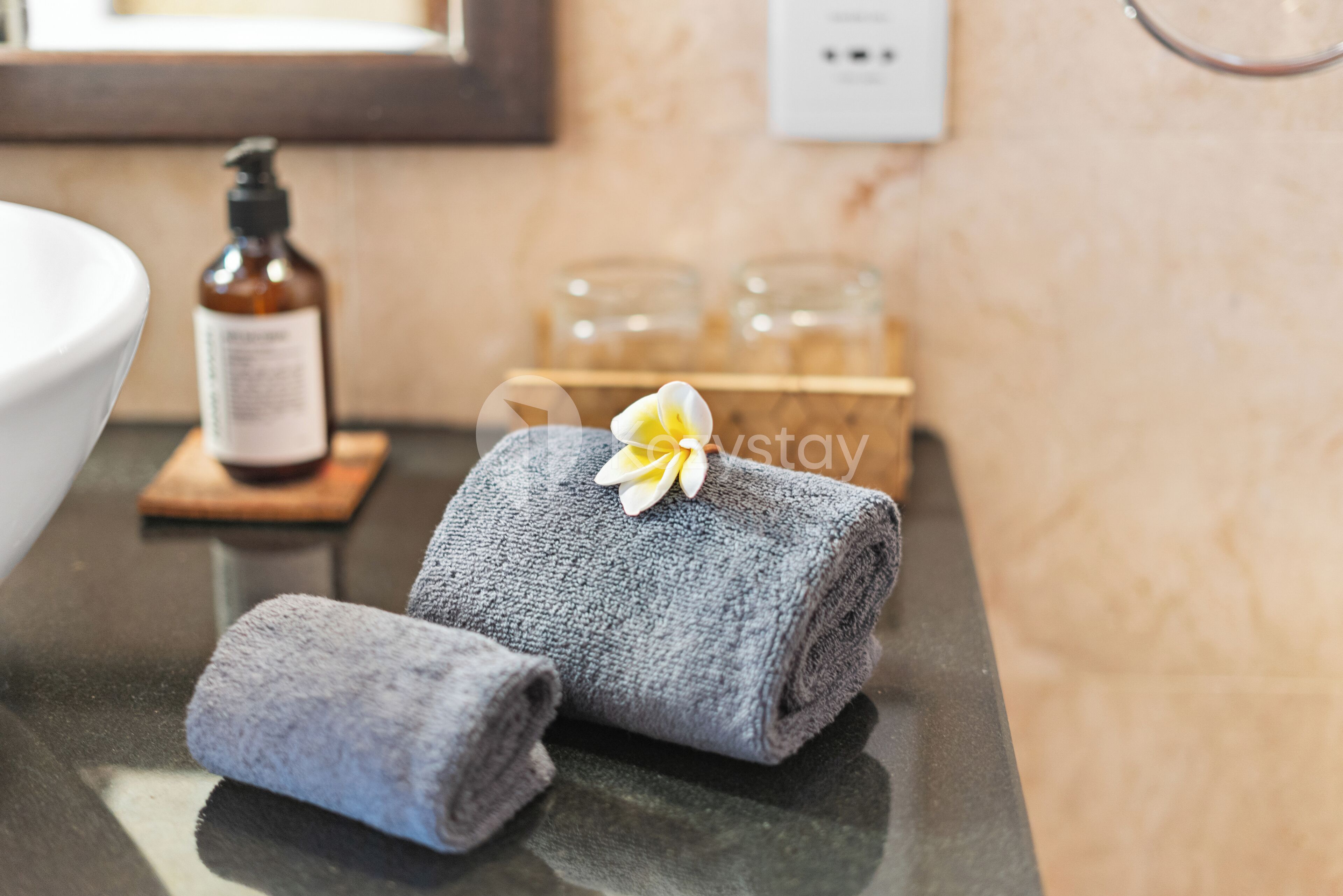 A bathroom with a towel and a flower on a counter, a bottle of soap, and a mirror.
