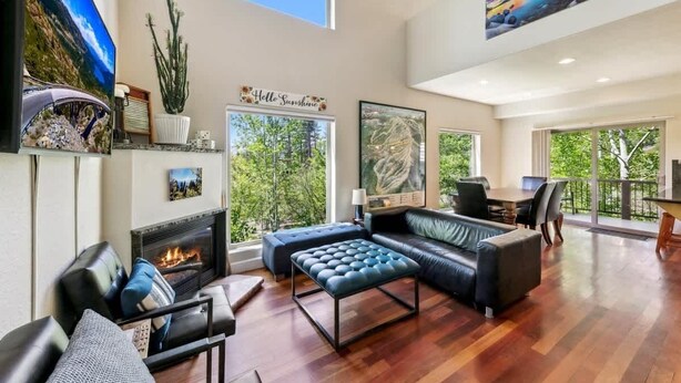 A spacious living room with a fireplace, leather sofa, and a dining area with a view of the outdoors. - Forest Mtn Lodge: Hot Tub, Game Room, Near Trail (South Lake Tahoe)