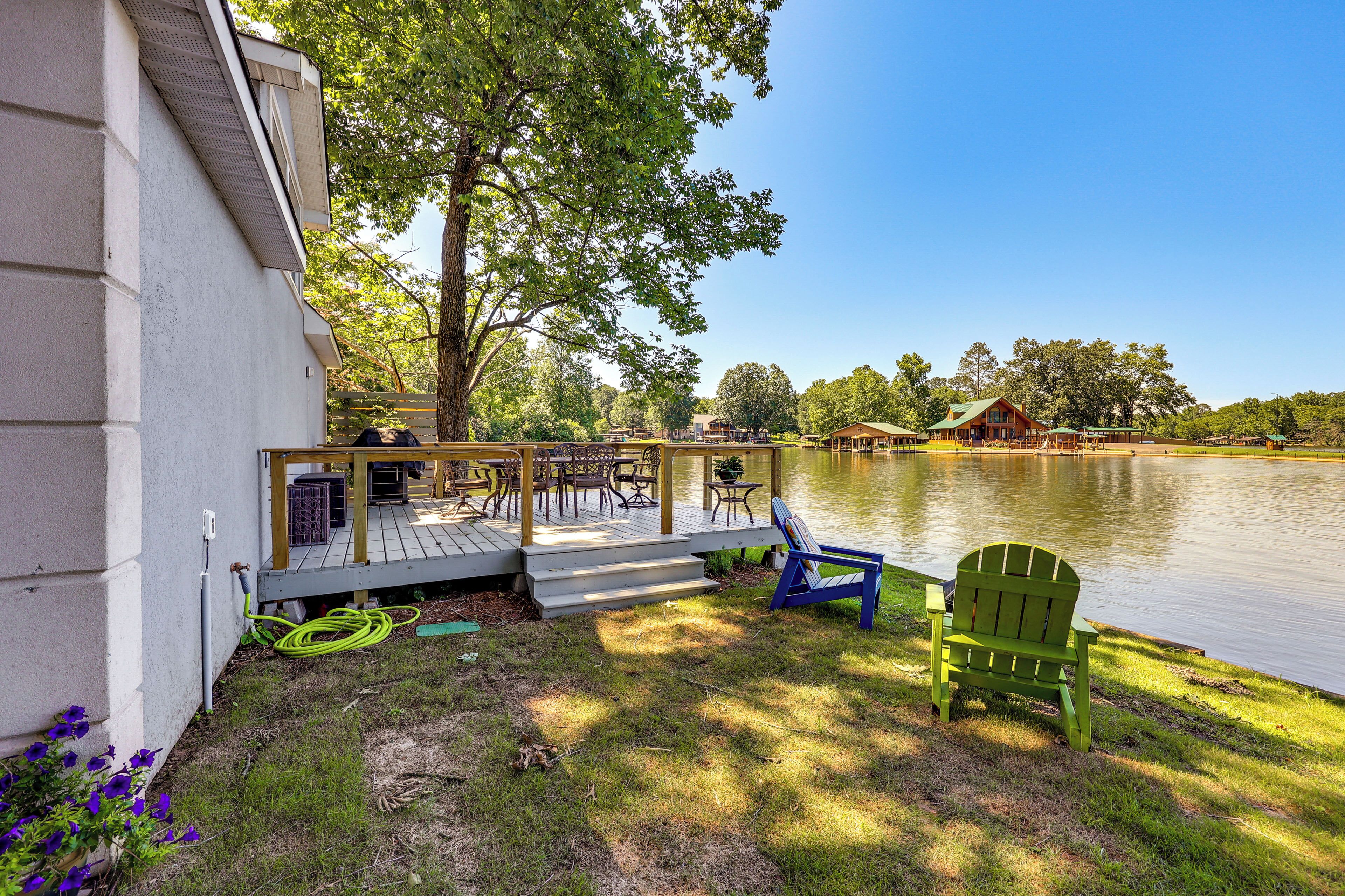 A lakeside deck with outdoor furniture and a wooden house in the background.