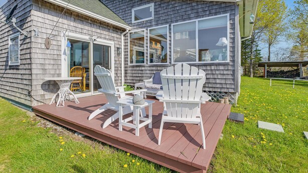 Une maison en bois dotée d’une terrasse, d’un espace salon extérieur et de grandes fenêtres.