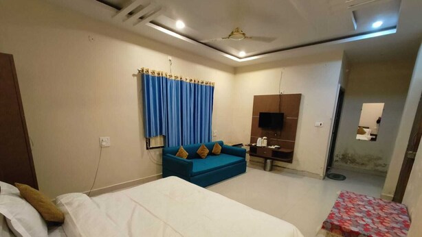 A hotel room with a bed, a sofa, a TV, and a small table. - Hotel Basant Palace (Gopadbanas)