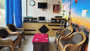 A reception area with a desk, chairs, a clock, and a wall mural. - Hotel Basant Palace (Gopadbanas)