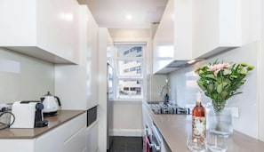 A narrow kitchen with a window, a coffee machine, a sink, and a vase with flowers. - Top Floor Darlinghurst Apt Sunroom Close To CBD (Sydney)