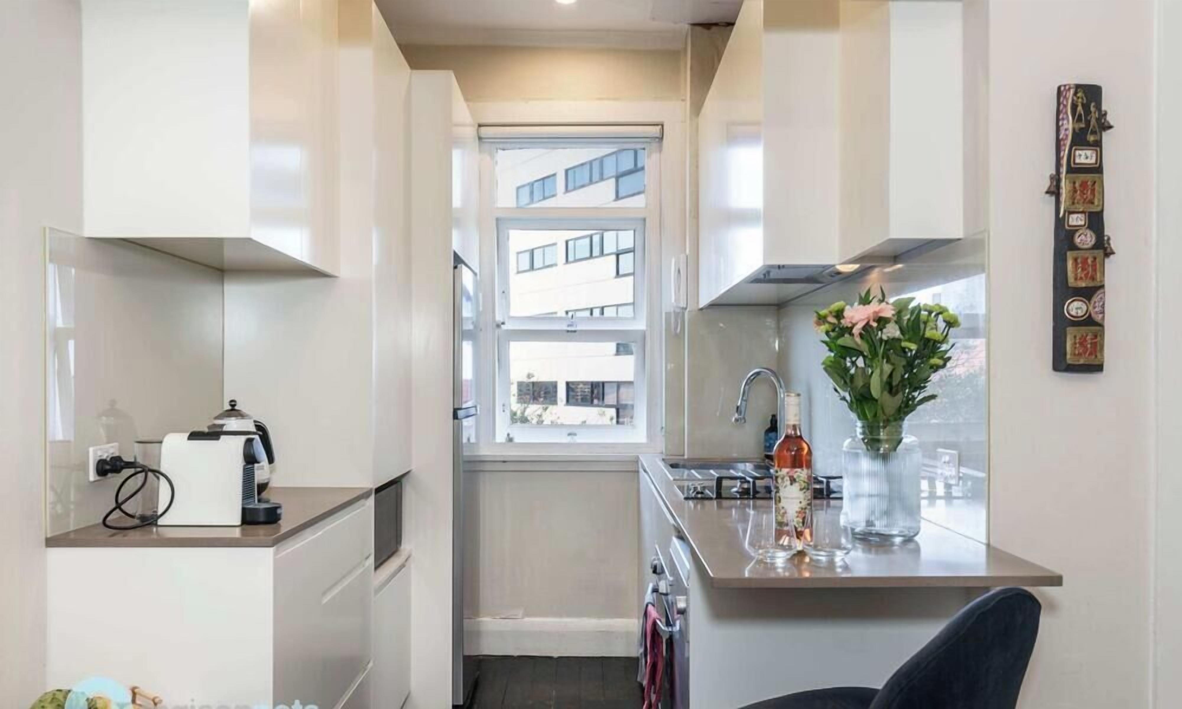 A compact kitchen with a window, a coffee machine, and a vase with flowers.