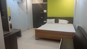 A bedroom with a bed, a bedside table, a wardrobe, a mirror, and a wall-mounted fan. - HOTEL ROYAL RESIDENCY (Shillong)