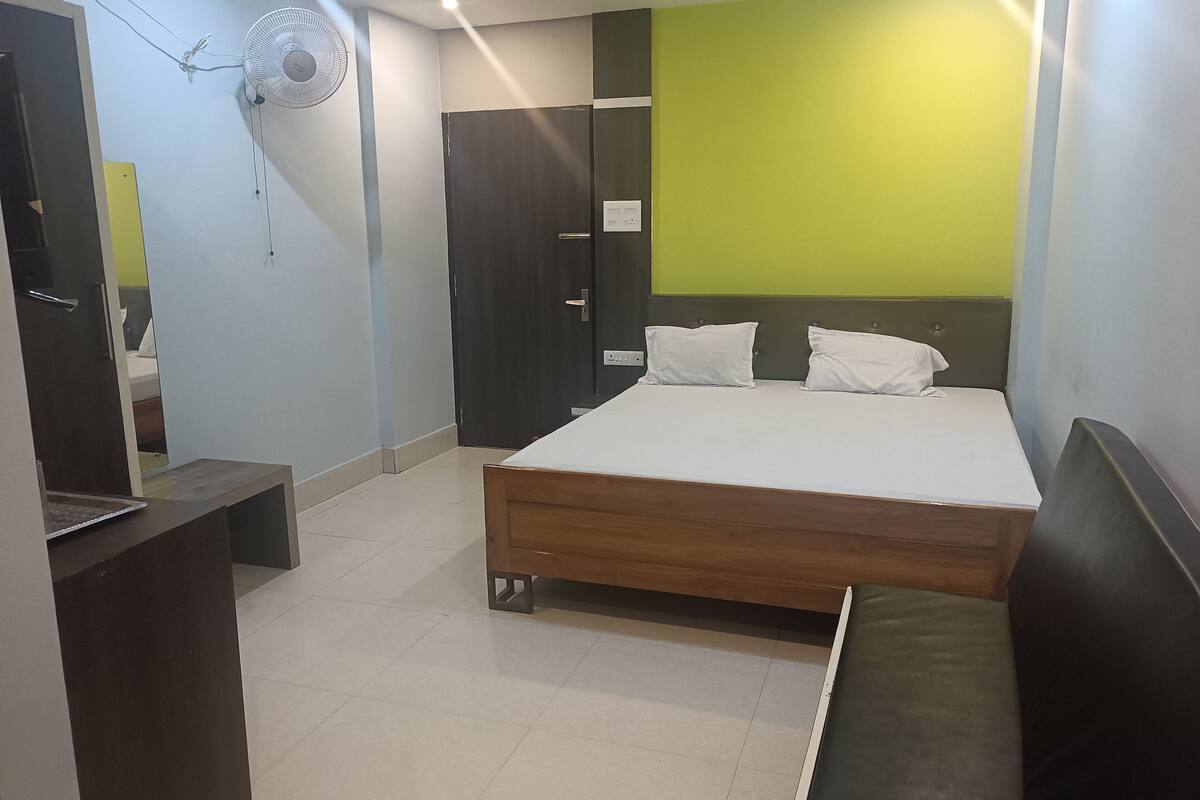 Un dormitorio con cama, mesita de noche, armario, espejo y ventilador de pared.