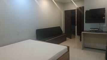 A modern bedroom with a bed, a dark sofa, a TV mounted on the wall, and a small desk with a computer.