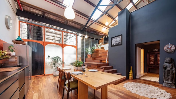 A modern kitchen with wooden cabinets, a dining table, and a staircase leading to a loft area. - Spacious Warehouse Conversion, 2 Bdrms & Parking (Footscray)