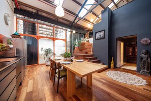 A modern kitchen with wooden cabinets, a dining table, and a staircase leading to a loft area. - Spacious Warehouse Conversion, 2 Bdrms & Parking (Footscray)