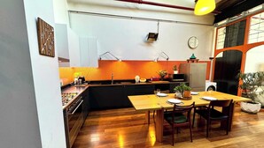A modern kitchen with a wooden dining table and chairs, a built-in oven, and a small island with a sink. - Spacious Warehouse Conversion, 2 Bdrms & Parking (Footscray)