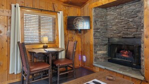 Une pièce chaleureuse avec une cheminée en pierre, des murs en bois, un téléviseur fixé au mur et une table à manger avec des chaises.