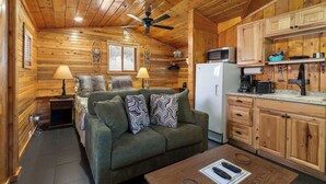 Une chambre confortable, aménagée dans le style d’un chalet, avec un intérieur en bois, un canapé agrémenté de coussins à motifs, une table à manger, un réfrigérateur et un four à micro-ondes.