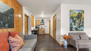 Un vaste espace de vie avec un canapé gris et un fauteuil gris, un plancher en bois et une cuisine en arrière-plan.