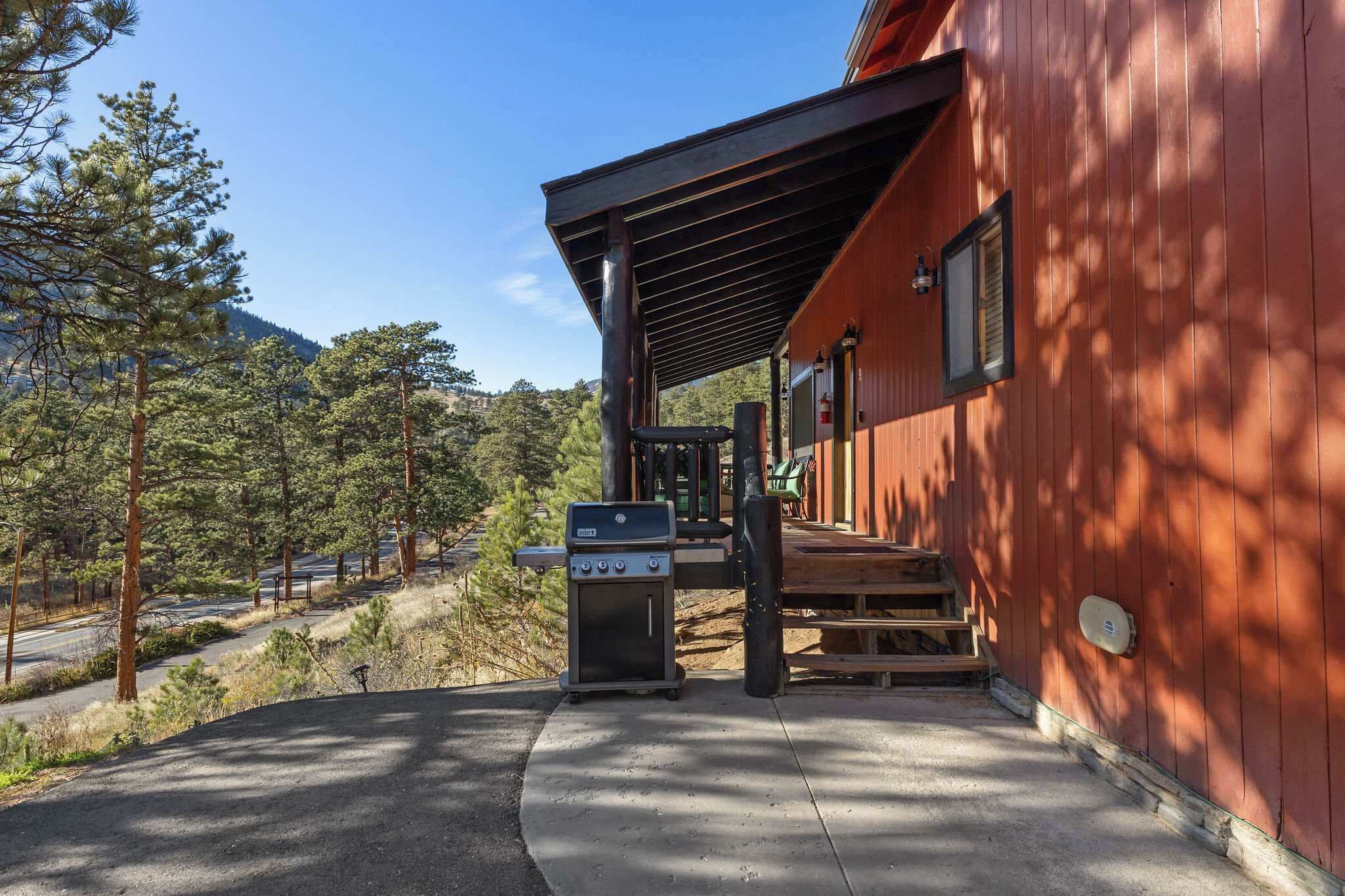 A red building with a covered porch, a grill, and a staircase leading to a door.