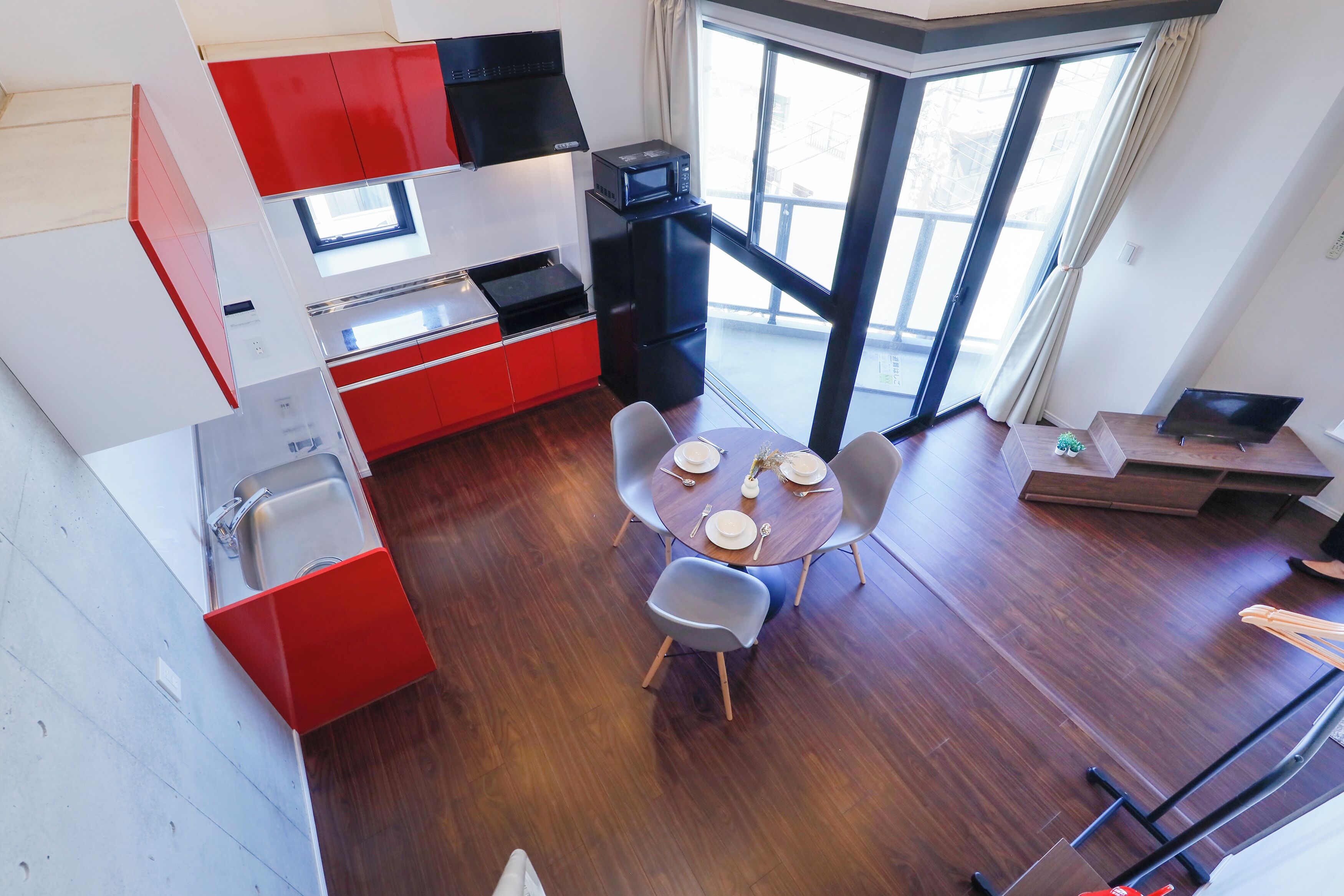 Une cuisine compacte avec des meubles rouges et blancs, un four à micro-ondes et un évier. On y trouve un coin repas avec une table et des chaises, ainsi qu’un ordinateur portable posé sur une petite table.