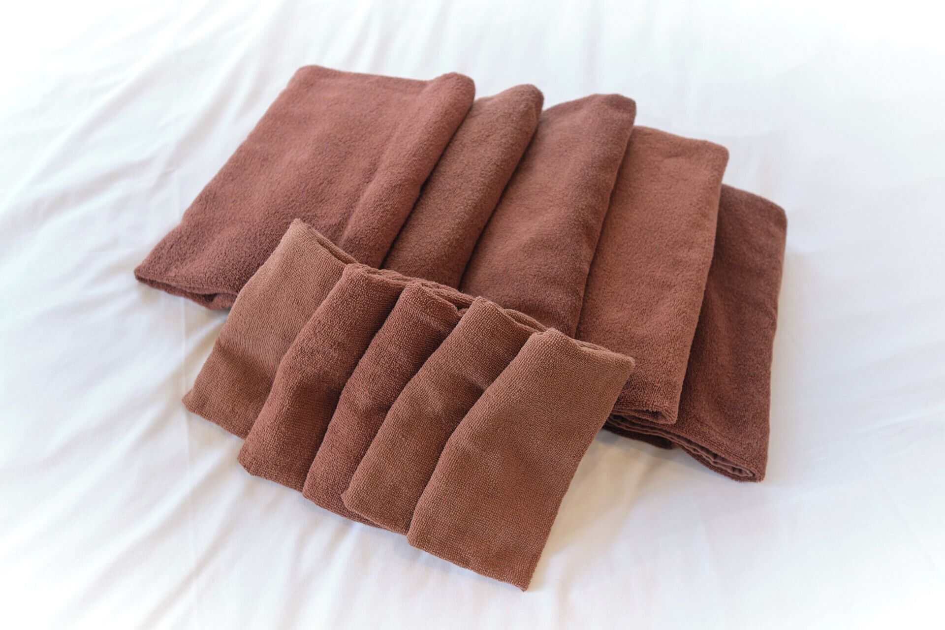 A neatly folded brown towel on a white bed.