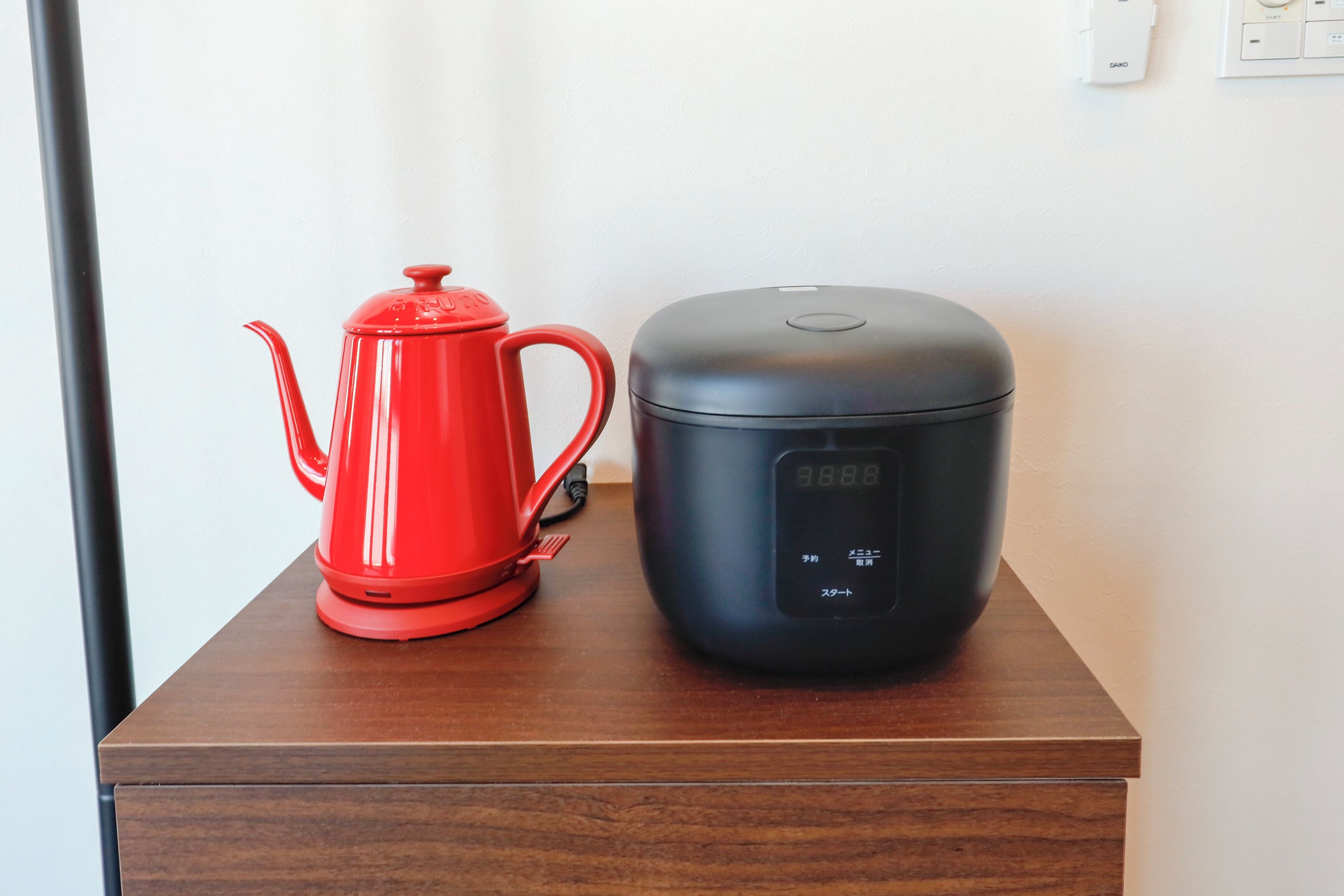 Una tetera roja eléctrica y una cocedora de arroz negra sobre una mesa de madera.