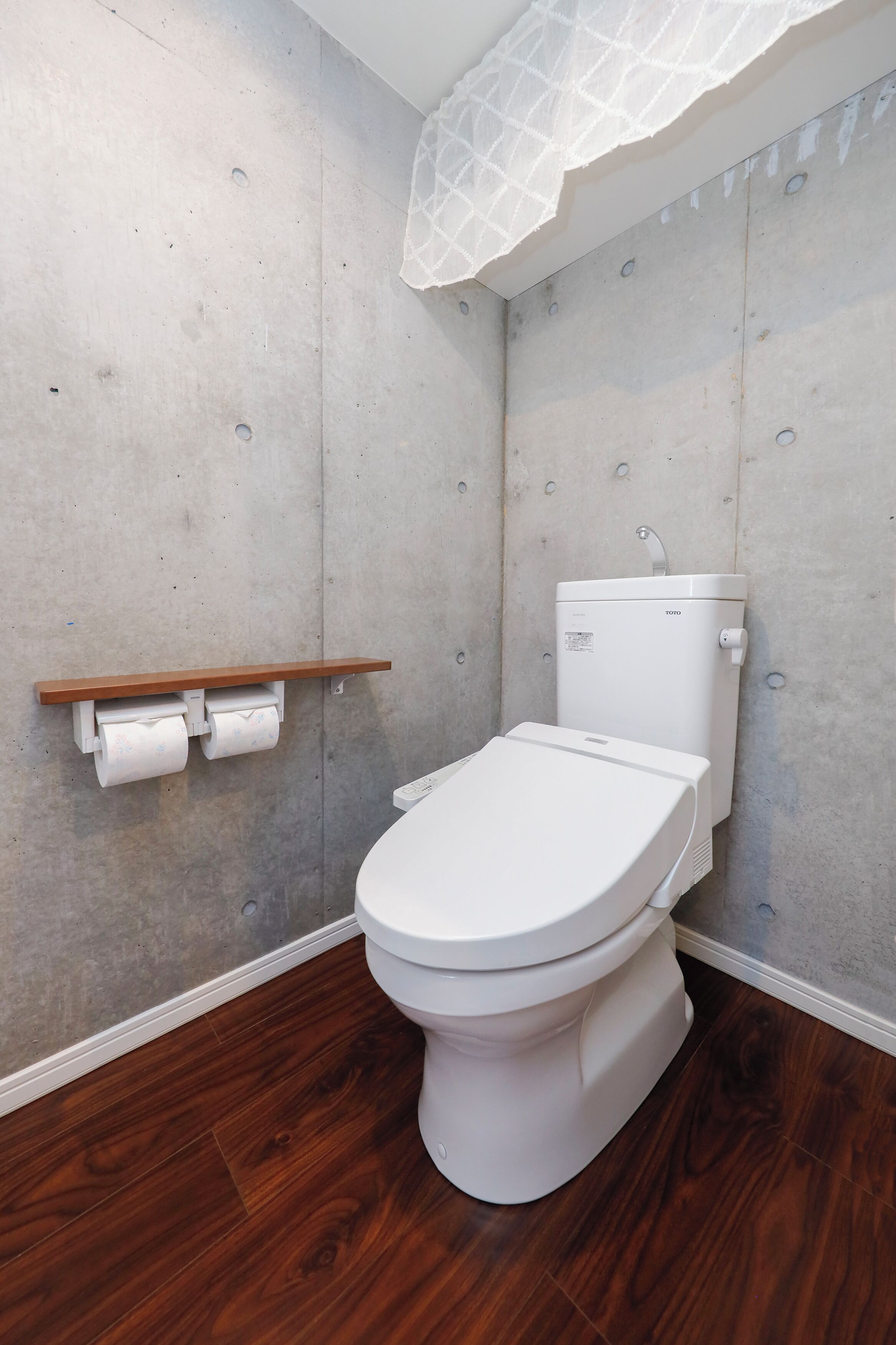 A modern bathroom with a white toilet, a wooden shelf with toilet paper, and a concrete wall.