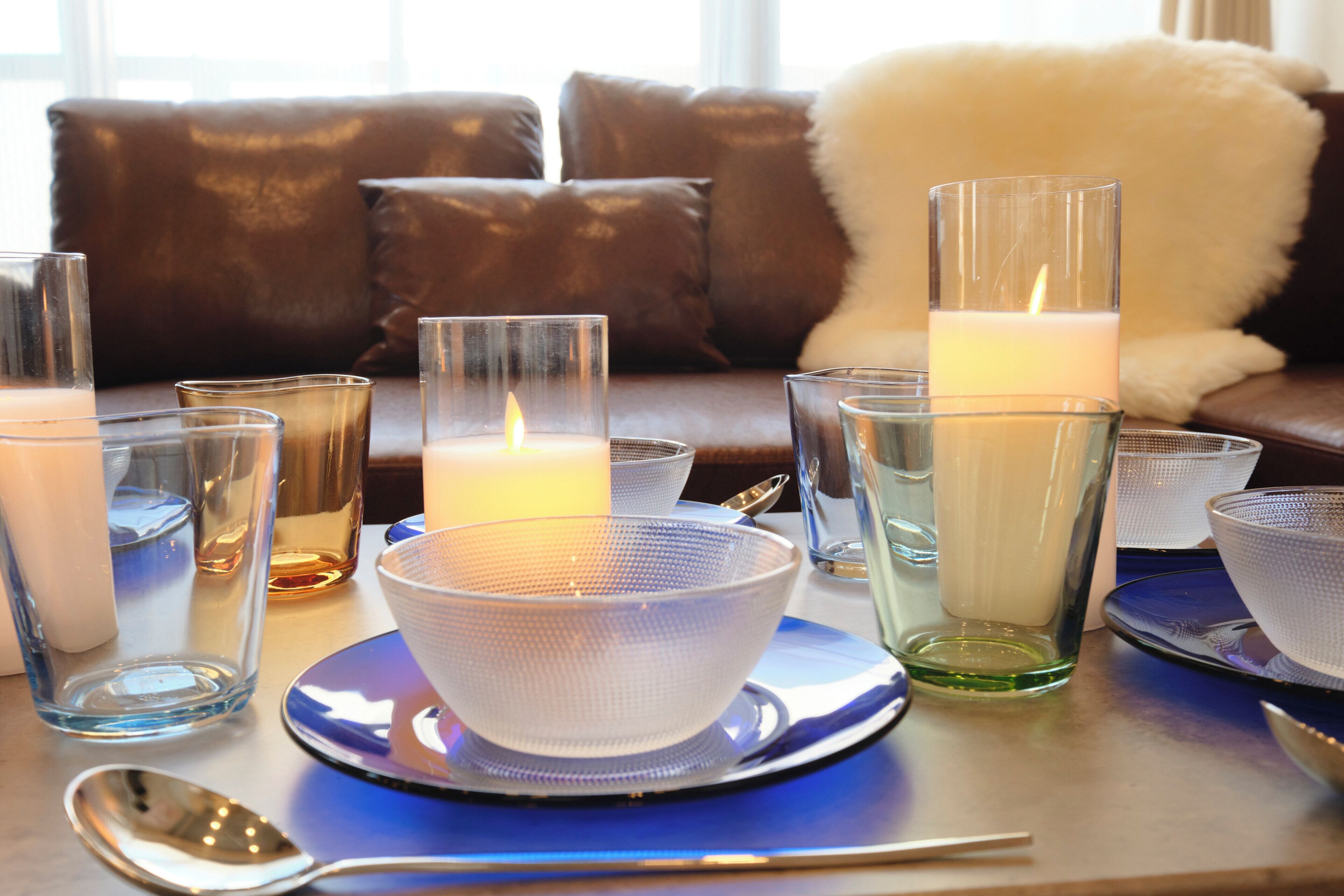 Una mesa dispuesta con cristalería transparente, un cuenco blanco y una vela.