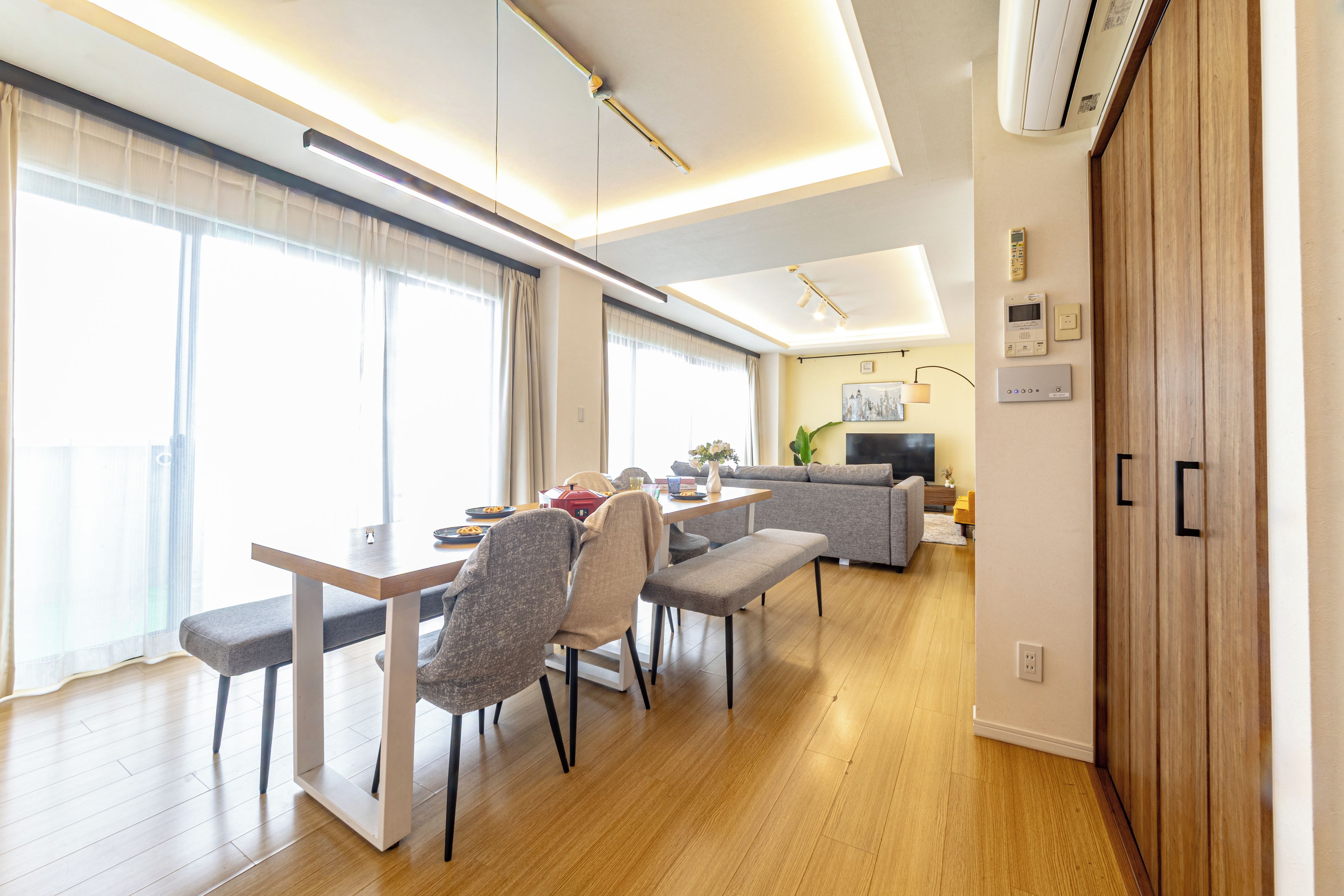 A modern living room with a dining area, wooden flooring, and a large window.