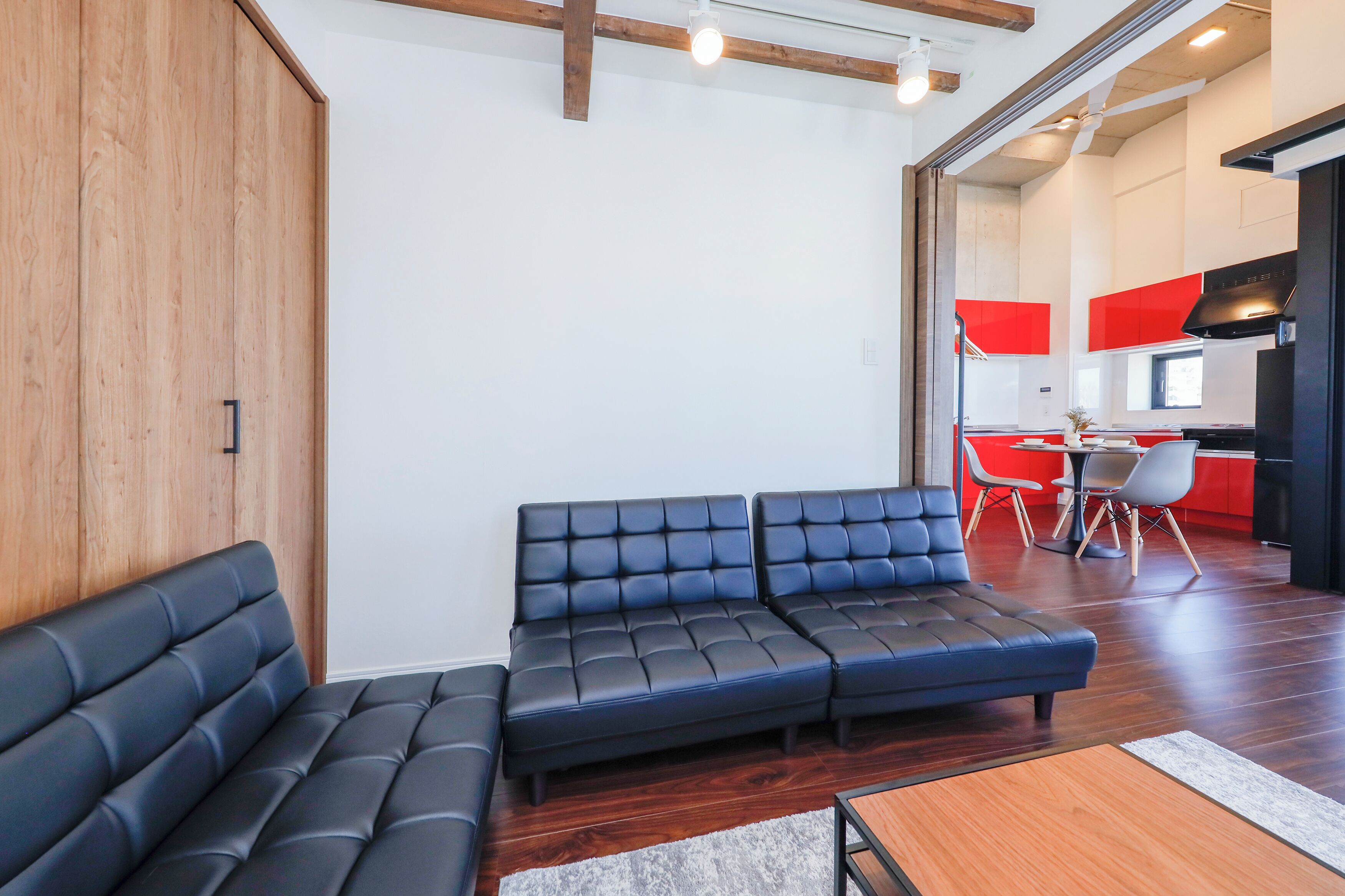 A modern living room with a sectional sofa, wooden flooring, and a kitchen area in the background.