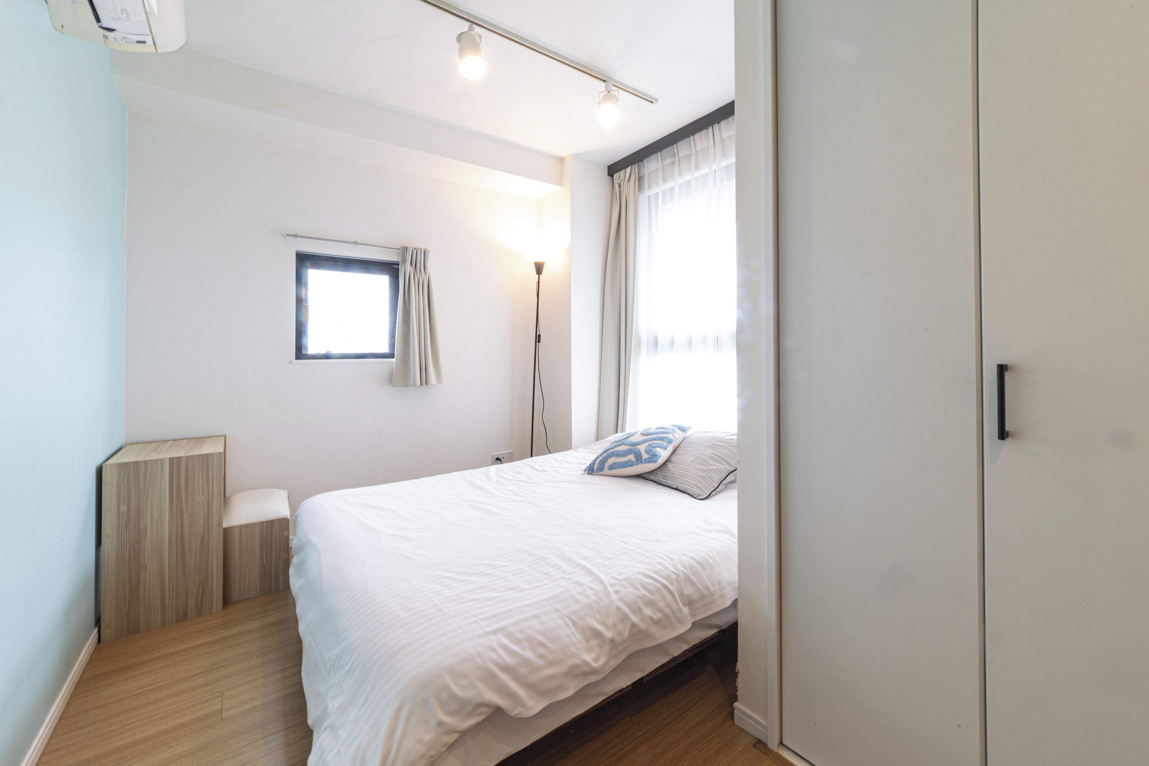 Una camera da letto con un letto, un comodino, un armadio, una finestra con tende e una lampada da terra.