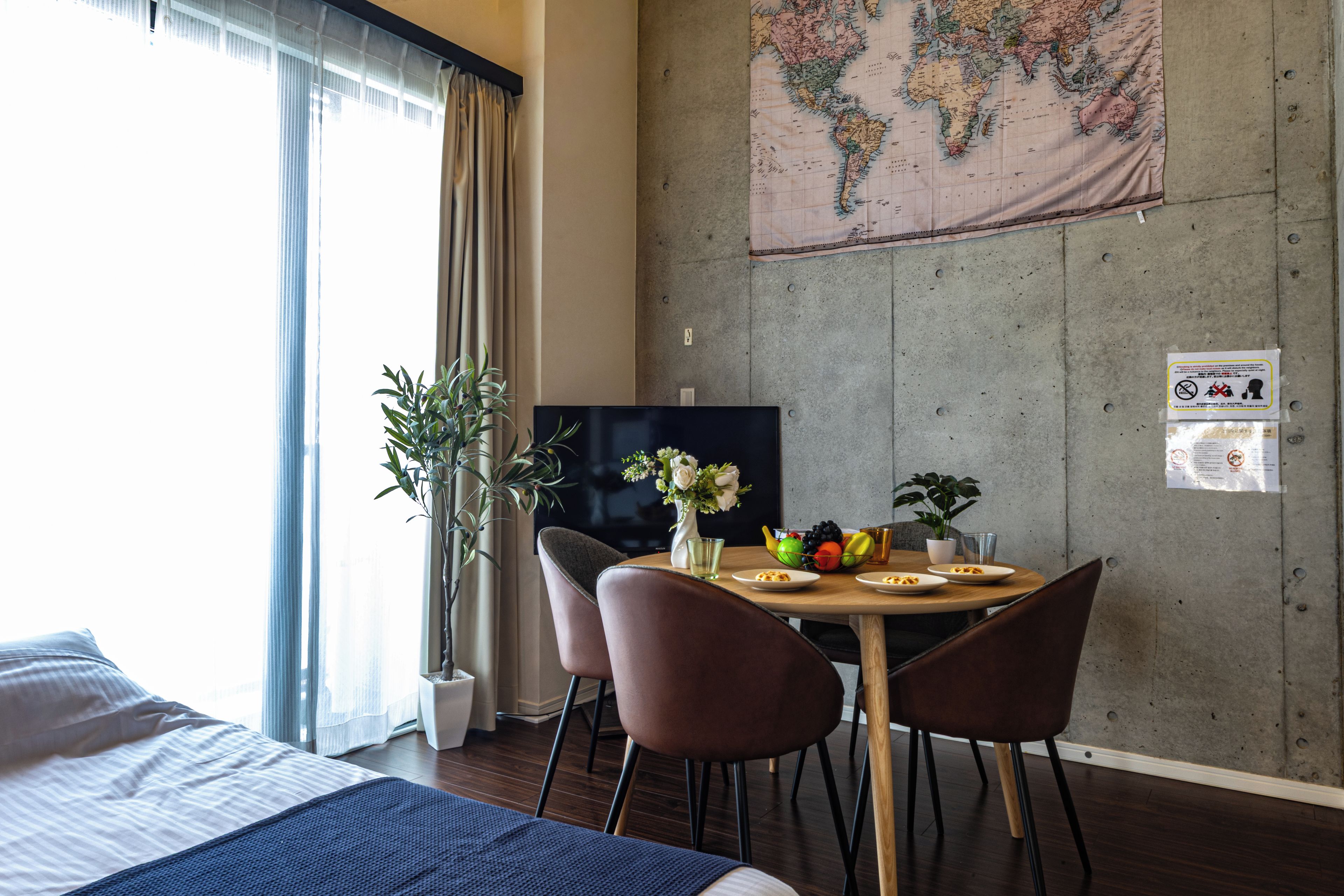 Une chambre d’hôtel avec un lit, une télévision, une table à manger avec des chaises, une plante et une carte du monde accrochée au mur.