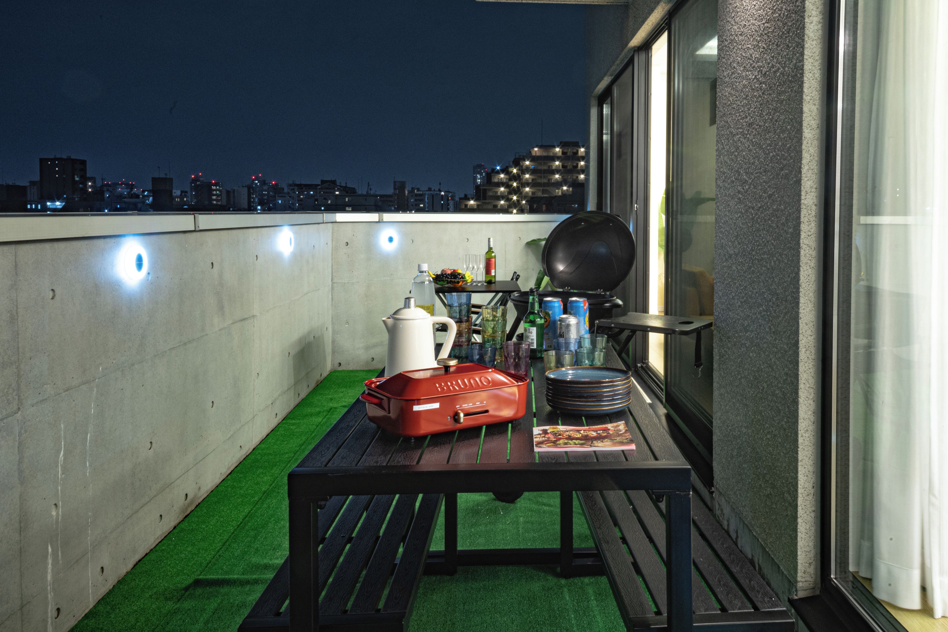 Eine Dachterrasse mit Esstisch, Grill und Blick auf die beleuchtete Stadt.