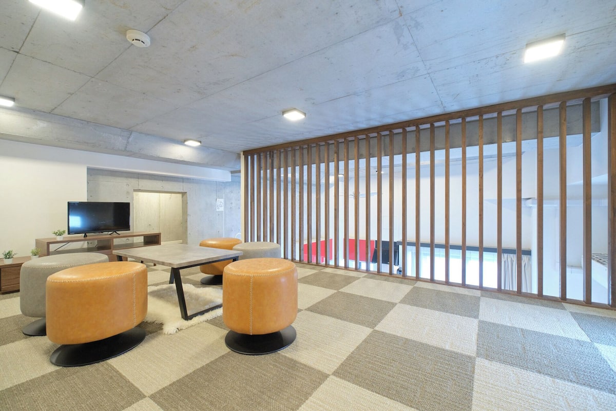 A modern office space with a large TV, two leather chairs, a wooden partition, and a checkered carpet.