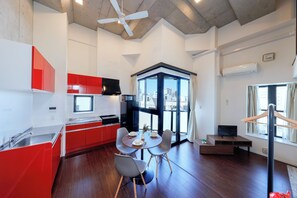 A modern kitchen with red cabinets, a dining area with a round table and chairs, and a large window with a city view. - Kiyosumi SOHO by Tranova (Tokyo)