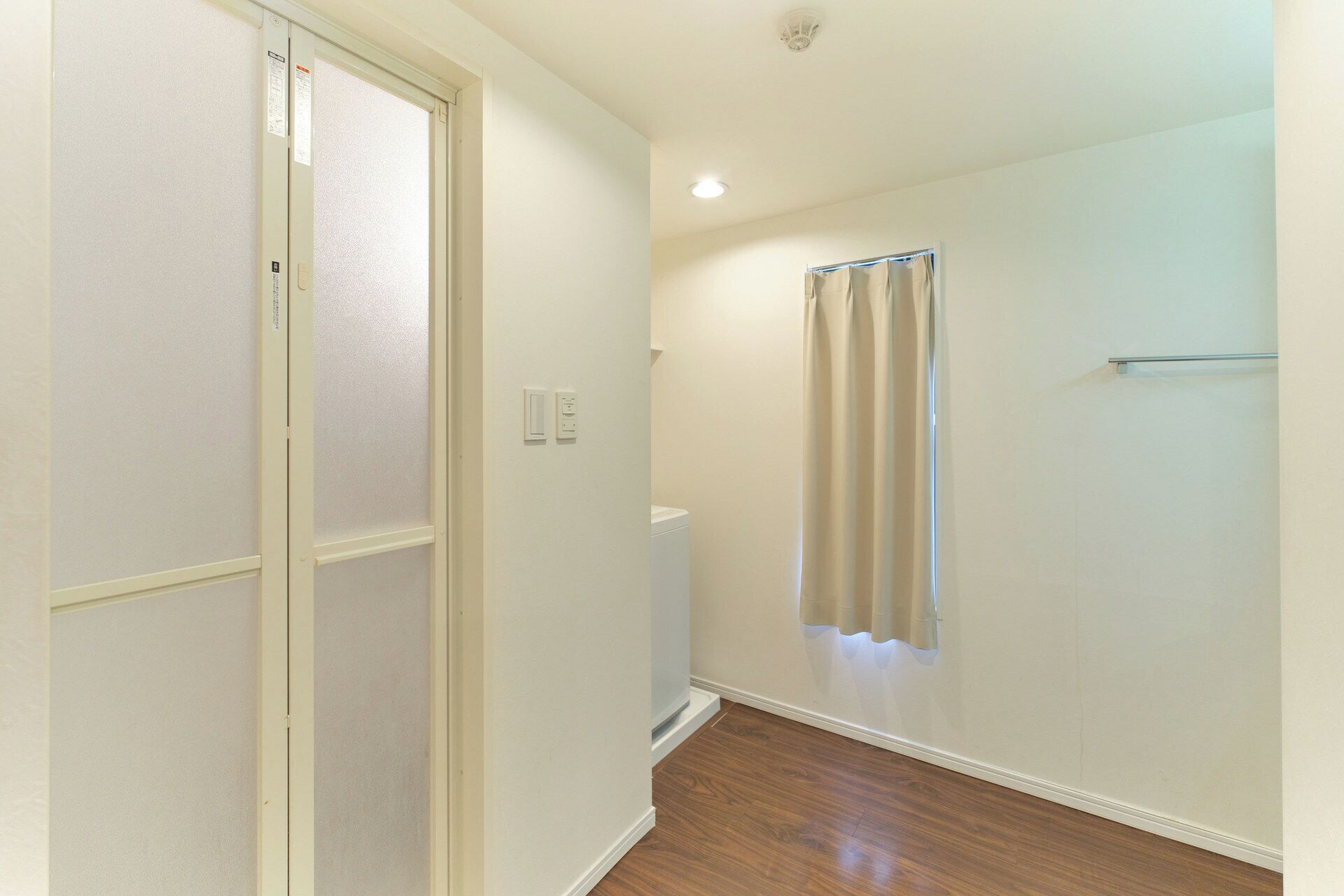 Un couloir étroit avec un plancher en bois, une porte en verre dépoli et une fenêtre avec un rideau.