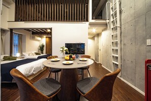 A modern hotel room with a dining area, a bed, a TV, and a balcony.