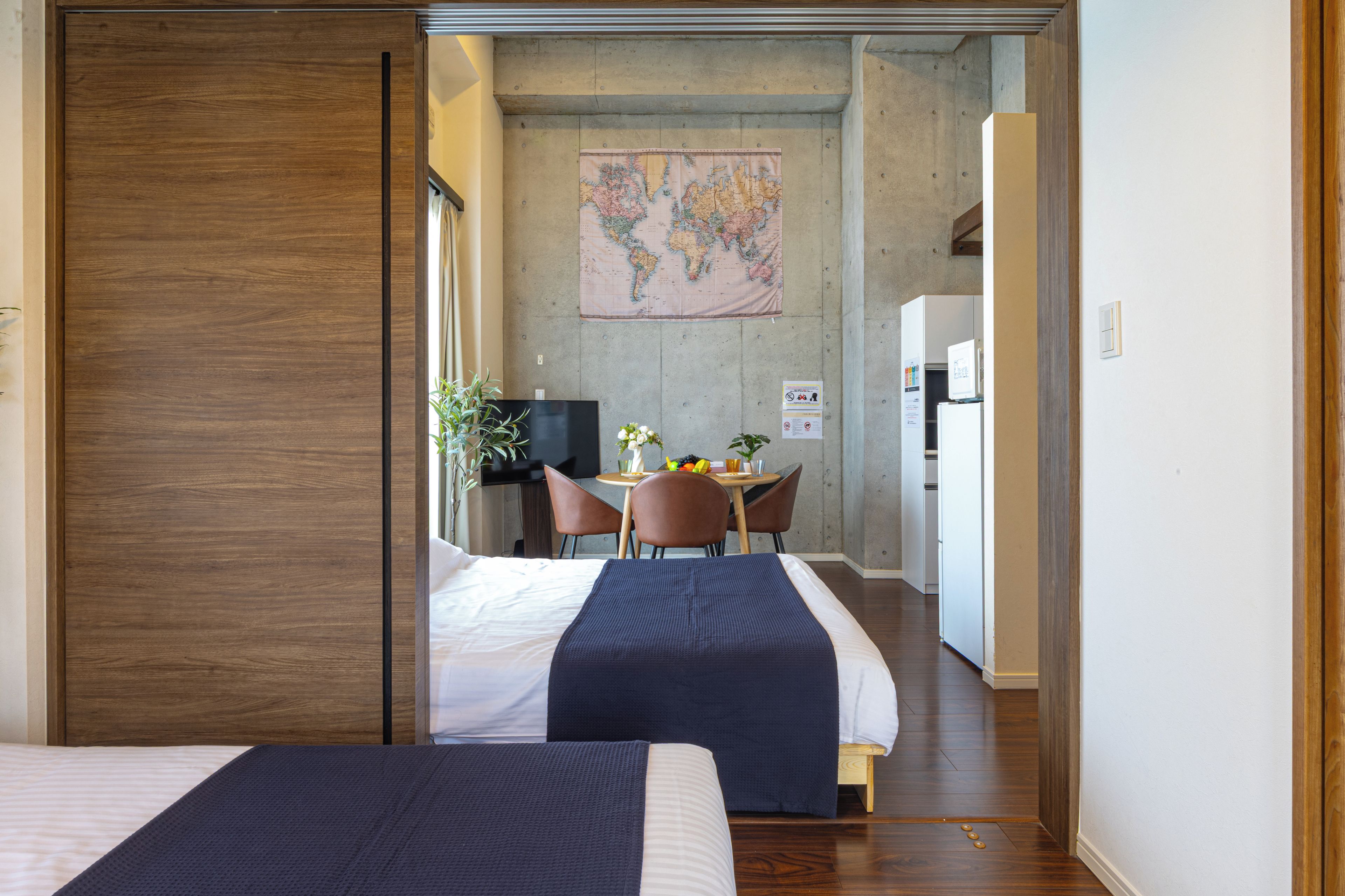 A hotel room with two beds, a desk with a chair, a small table with a plant, and a map on the wall.
